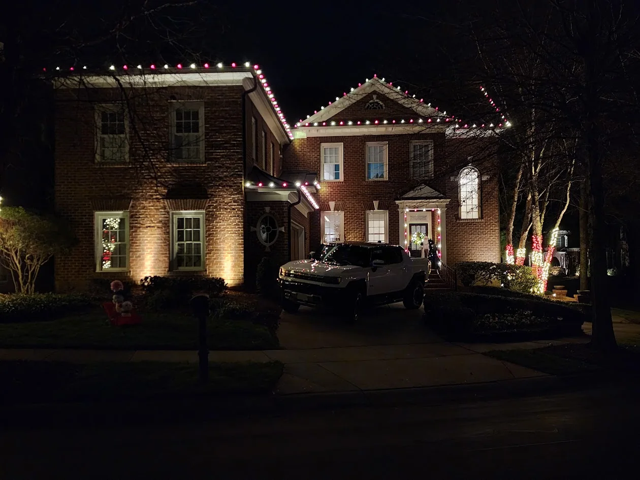 Red and warm white roofline, entry, and tree lighting on a brick home