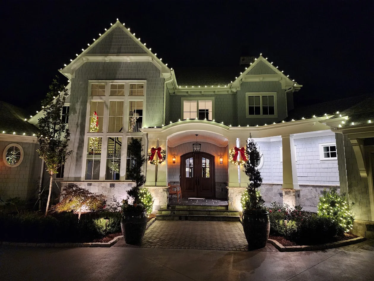 Layered warm white roofline lighting, wreaths, and landscape accents on a large home