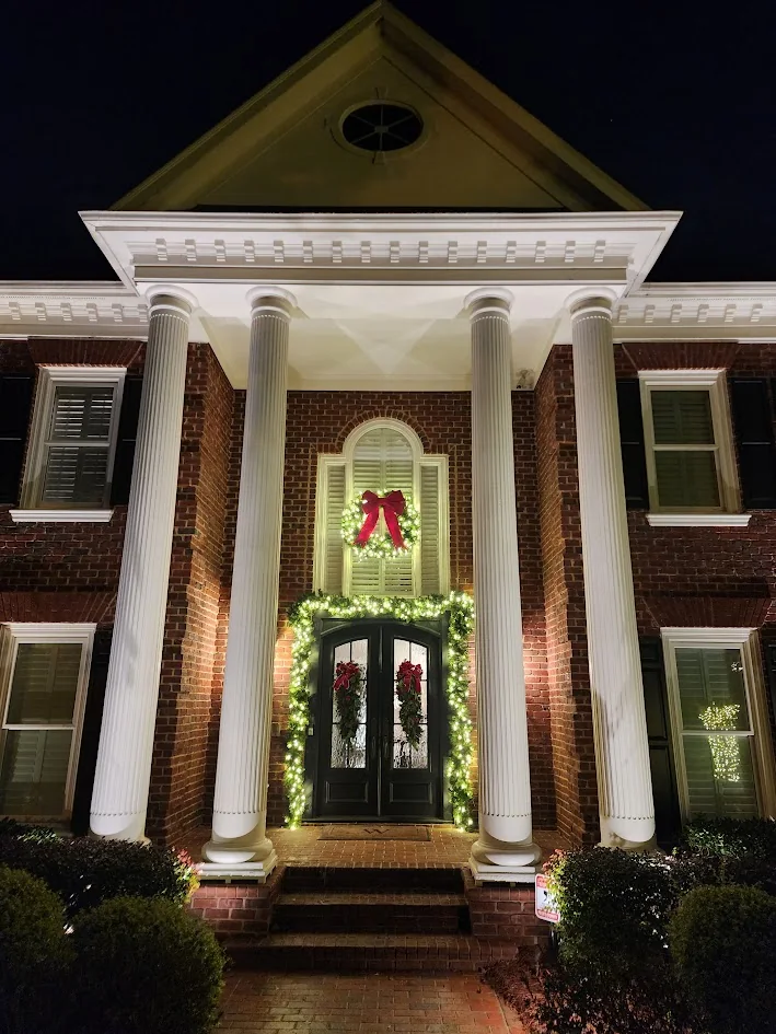 Lit garland and wreath at a columned entry after dark