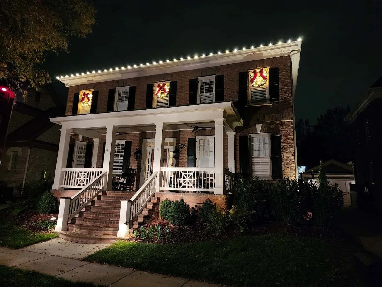 Warm white roofline lights and wreaths on a two-story brick home