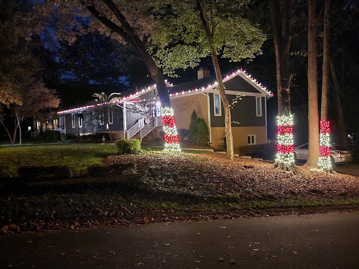 Red and warm white roofline and striped tree lighting on a Charlotte-area home