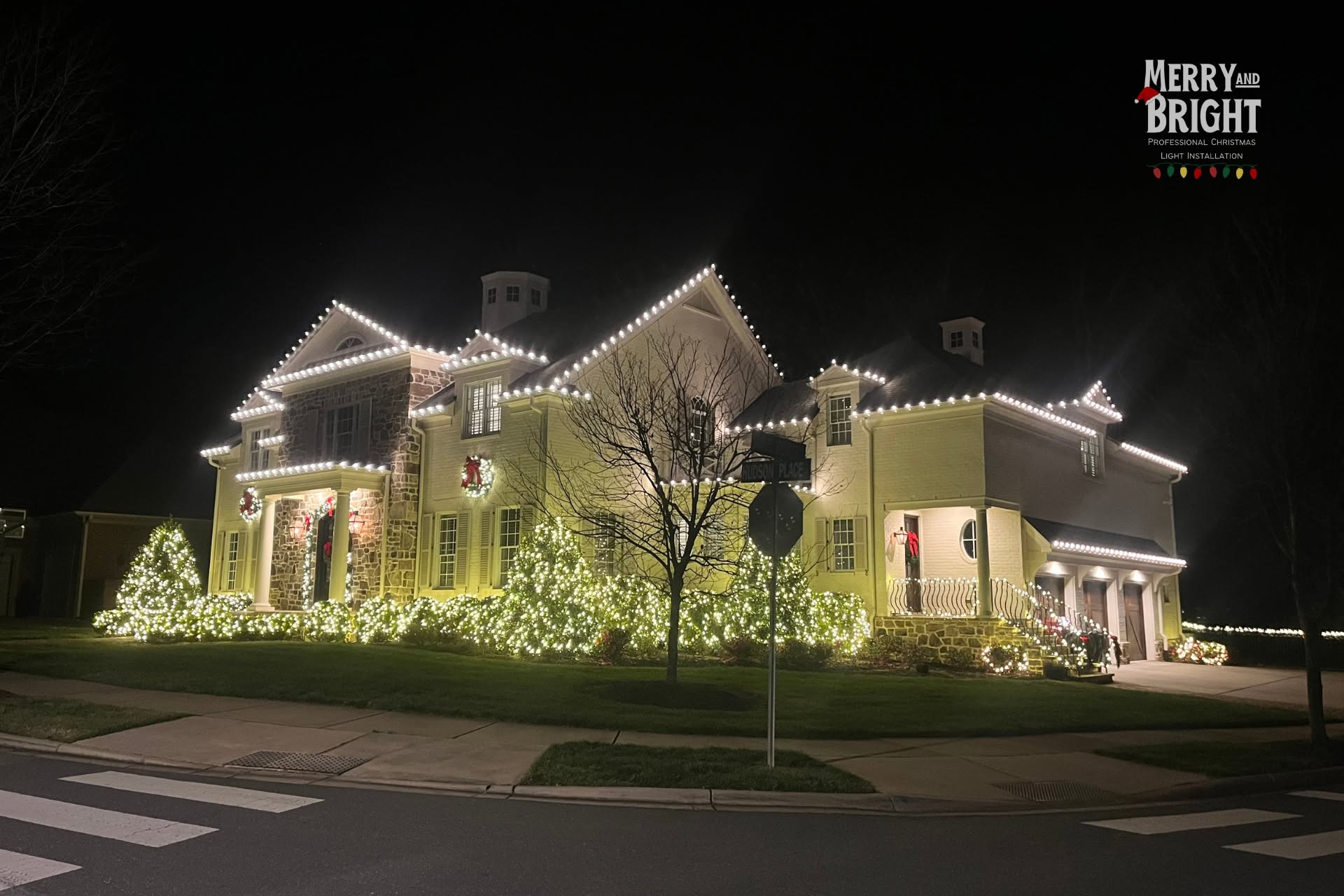 Layered warm white roofline lighting, wreaths, and illuminated landscaping on a Davidson home