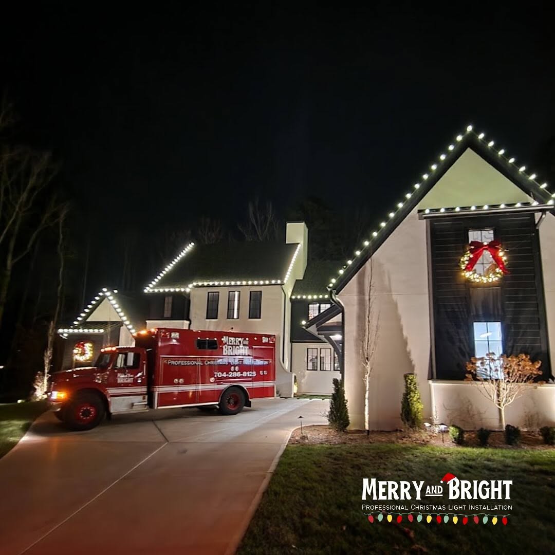 Warm white roofline lighting and large wreaths on a Davidson home