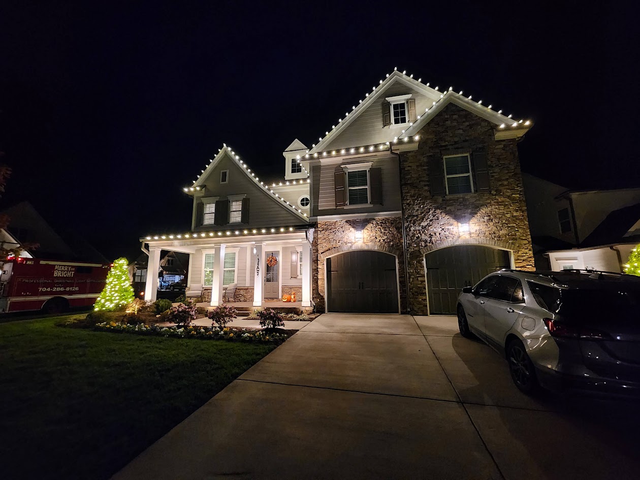 Warm white roofline and small-tree lighting on a Huntersville home