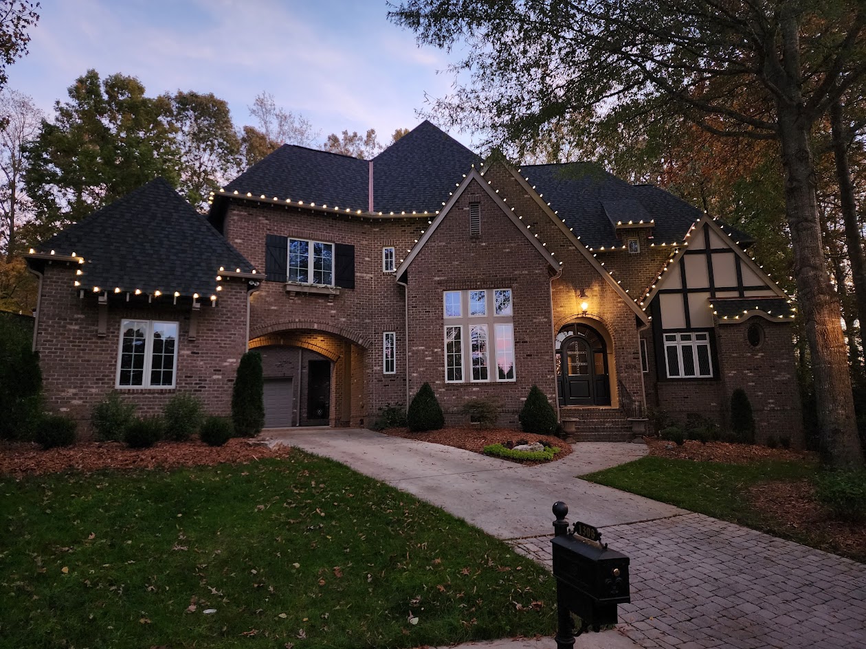 Warm white roofline lighting on a large brick home in Matthews