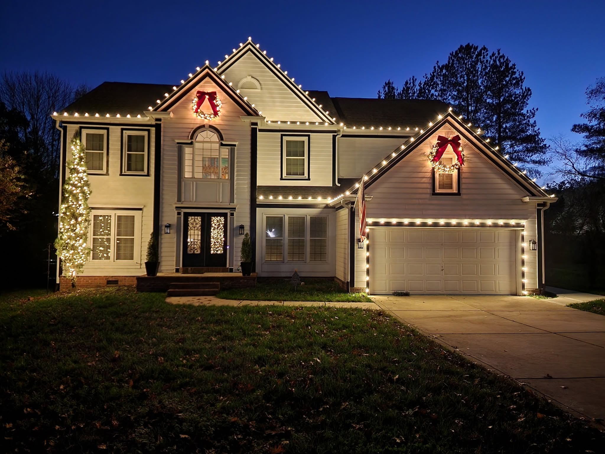 Warm white roofline lighting, wreaths, and a lit tree on a Charlotte home