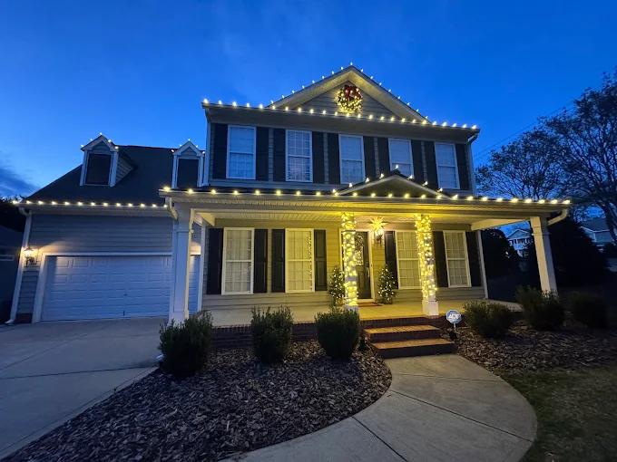 Warm white roofline and column lighting with a wreath above the entry