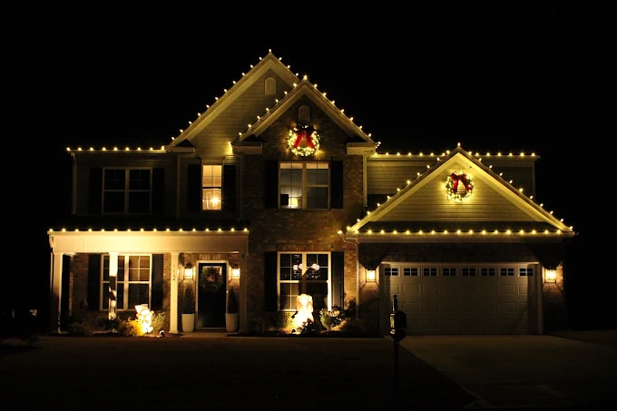 Warm white roofline lighting and wreaths across a Troutman home