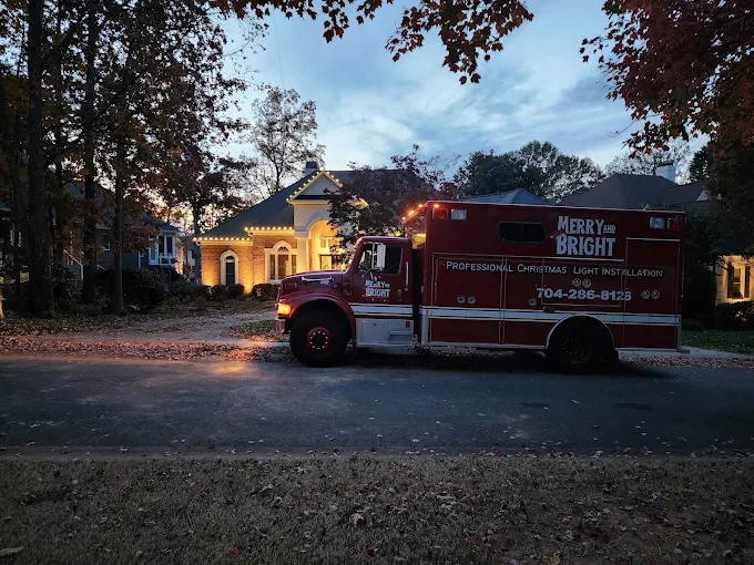 Merry & Bright truck at a home with a warm-white roofline at dusk