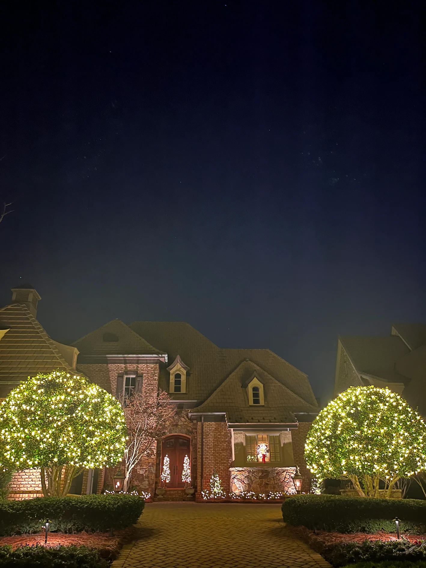 Large shrubs covered in warm white Christmas lights outside a home